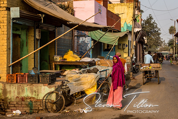 Woman sweeps the street in front of her shop.